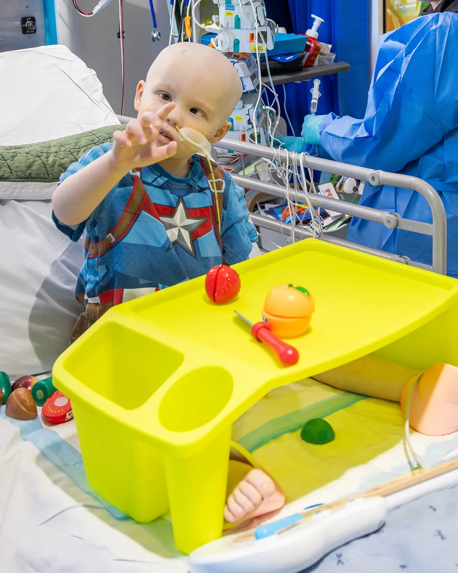 A little boy in a hospital bed waving