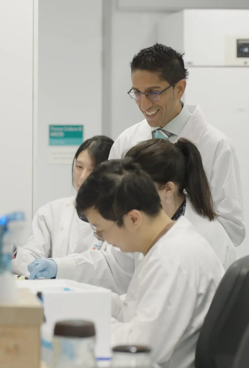 A lead researcher in a lab with his team looking at a lab bench.