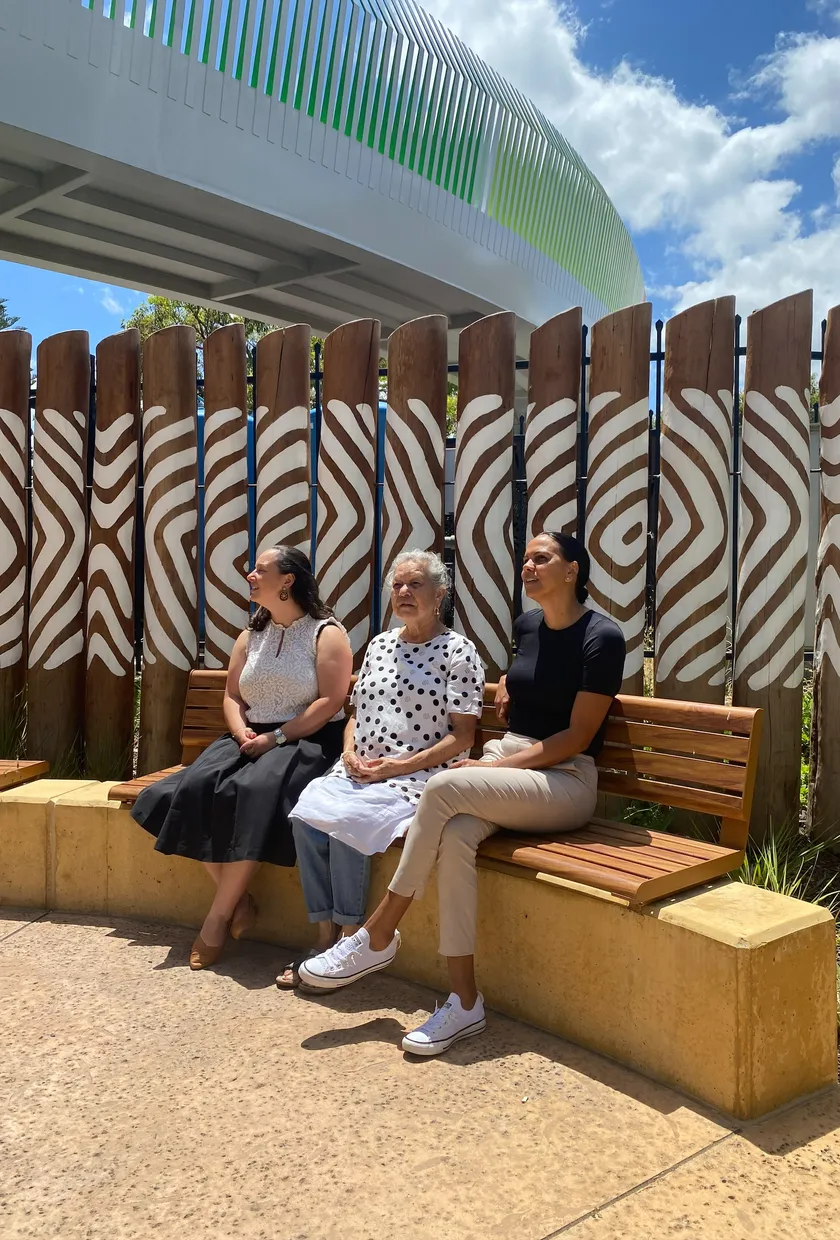 Three women sitting on a bench outside staring at the sky.