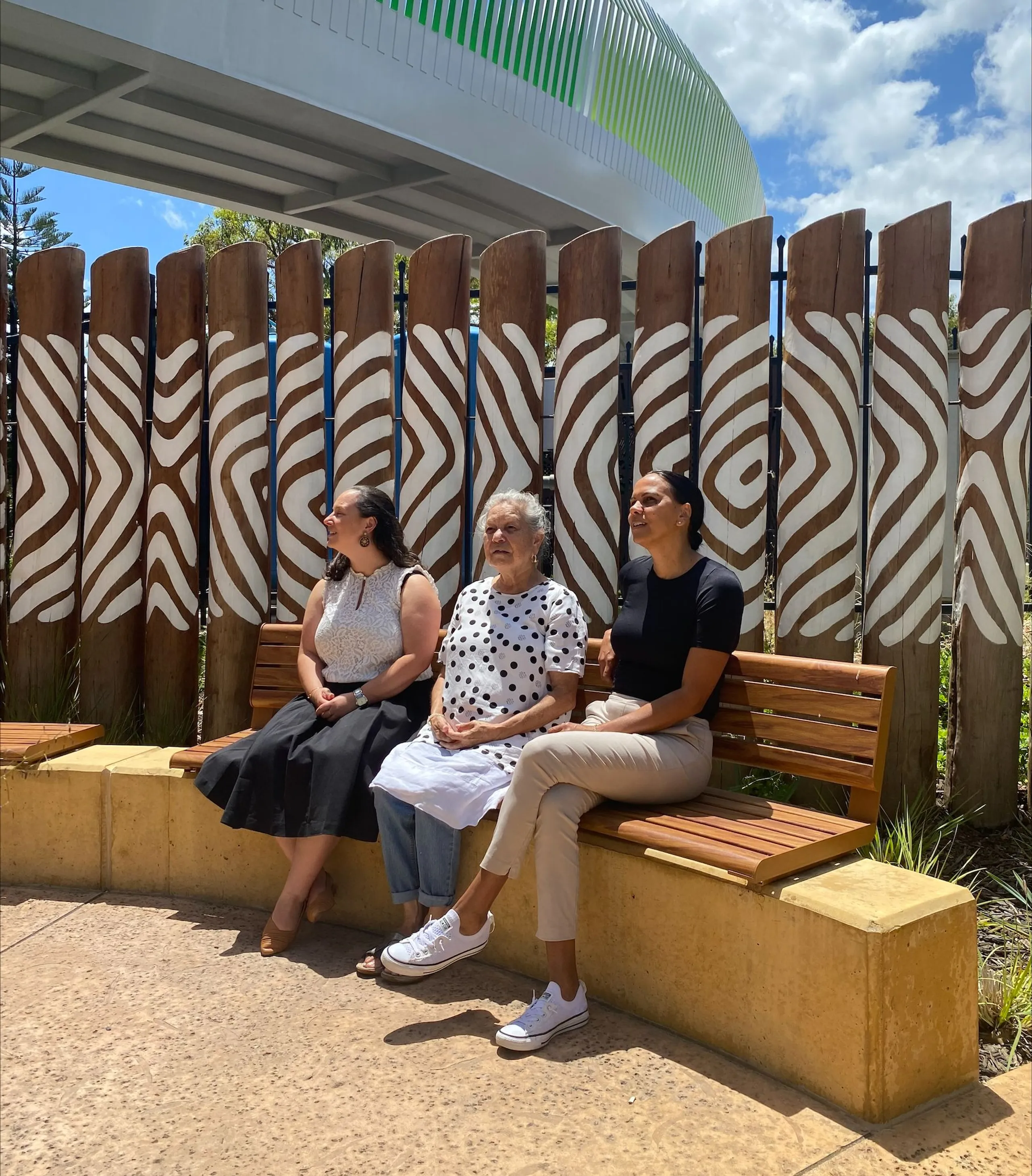 Three women sitting on a bench looking at the sky.