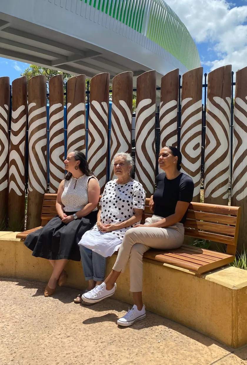 Three women sitting on a bench looking at the sky.