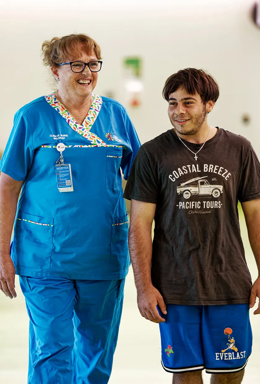 A clinical nurse walking and smiling with an adolescent boy, both smiling.