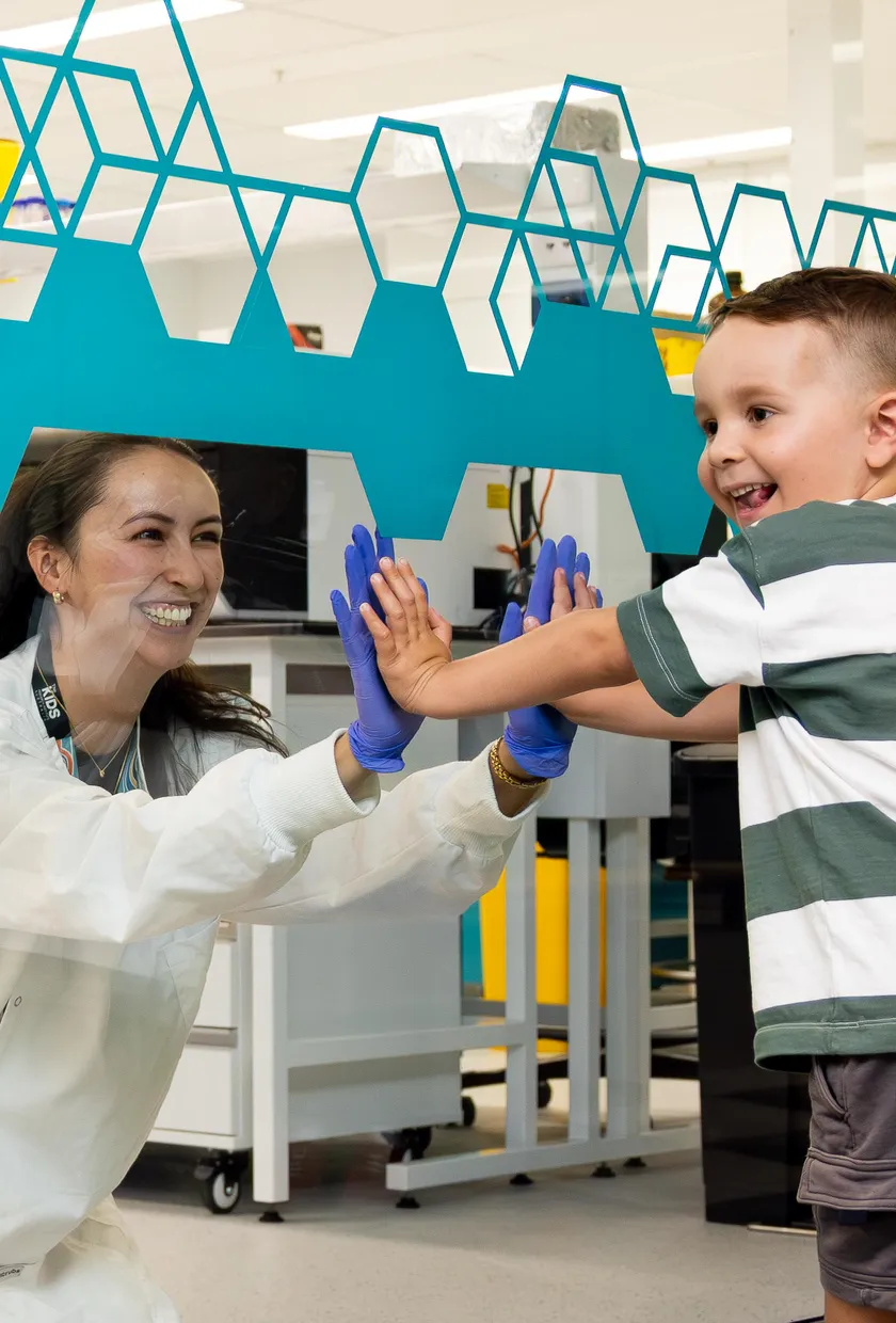 Scientist touching hands with young boy through glass.