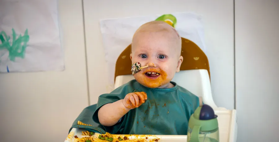 A baby with food on their face and a nose tube.