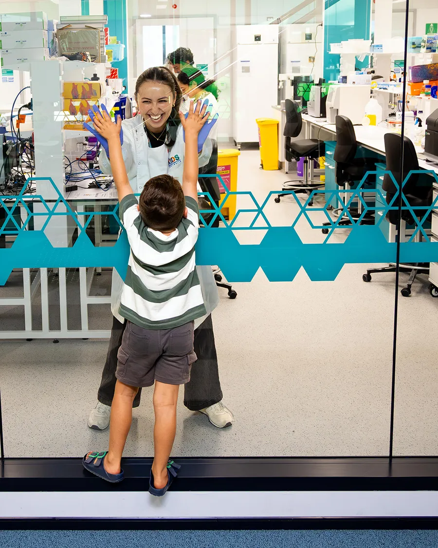 a young boy touching hands with a scientist through glass wall