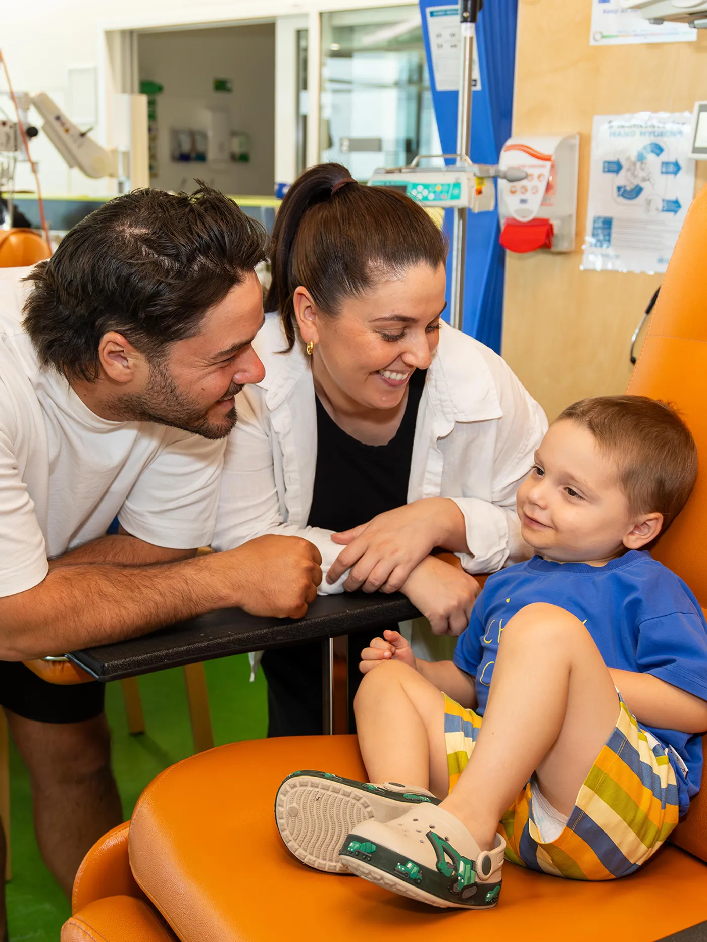 two parents smiling at their son in a big orange chair