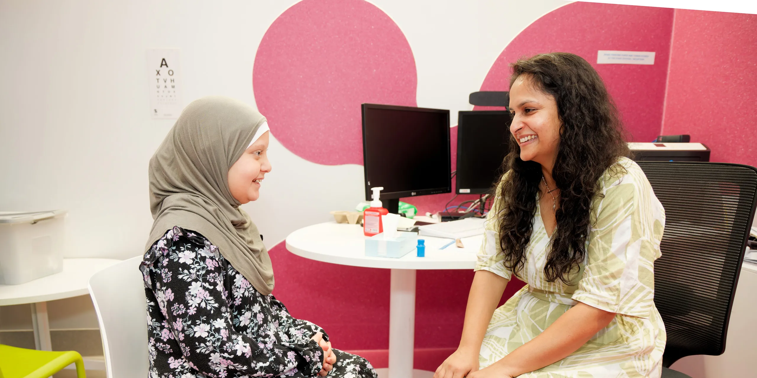 A cancer doctor sitting with a young girl, smiling and talking.