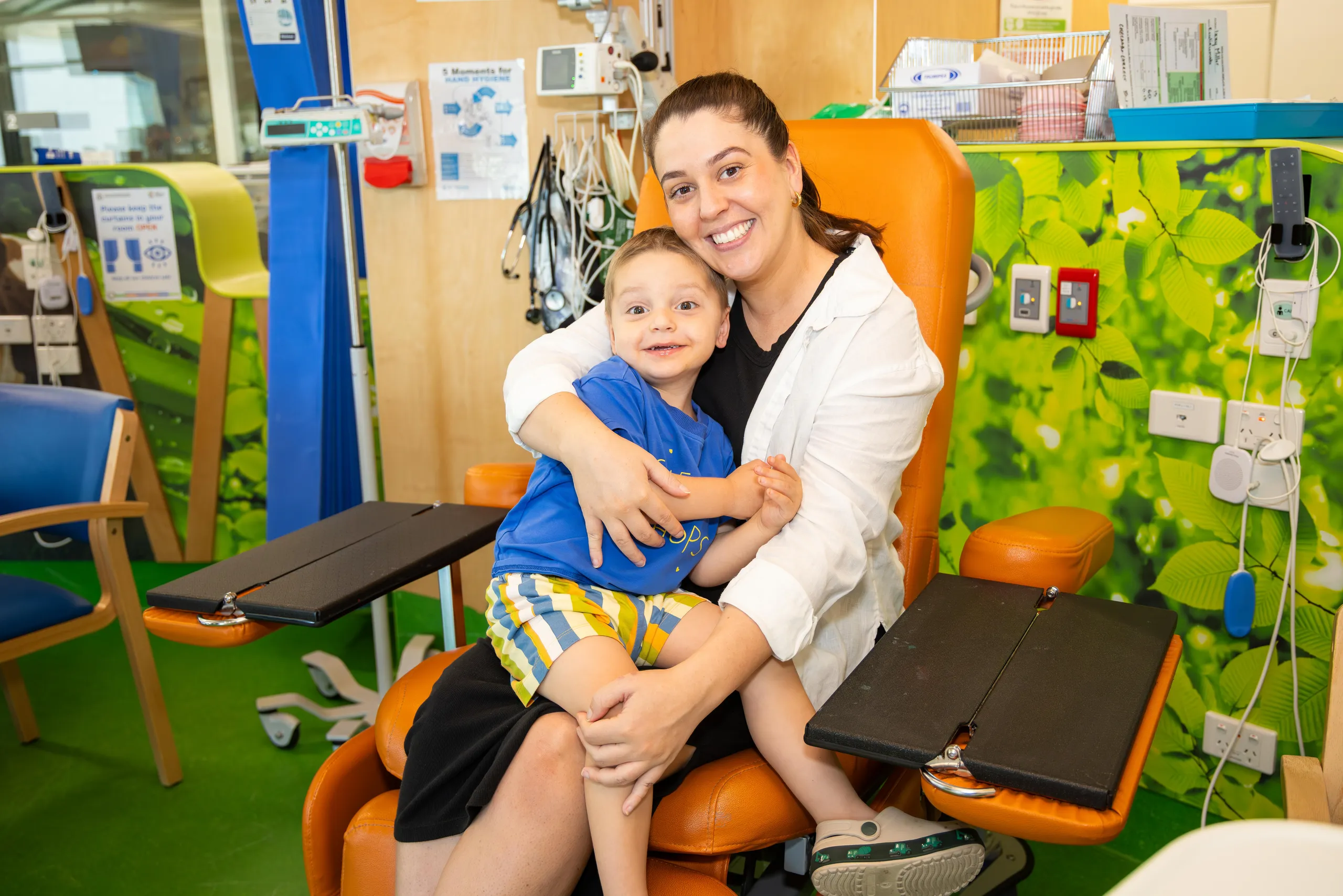 A little boy sitting on his mums lap in a chair, both smiling.