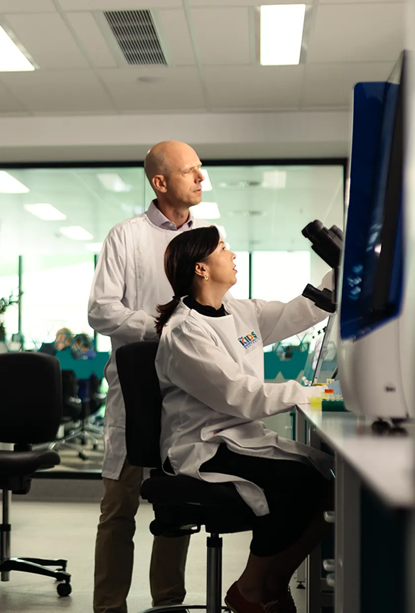 Two scientists in a lab looking at a screen next to a microscope.