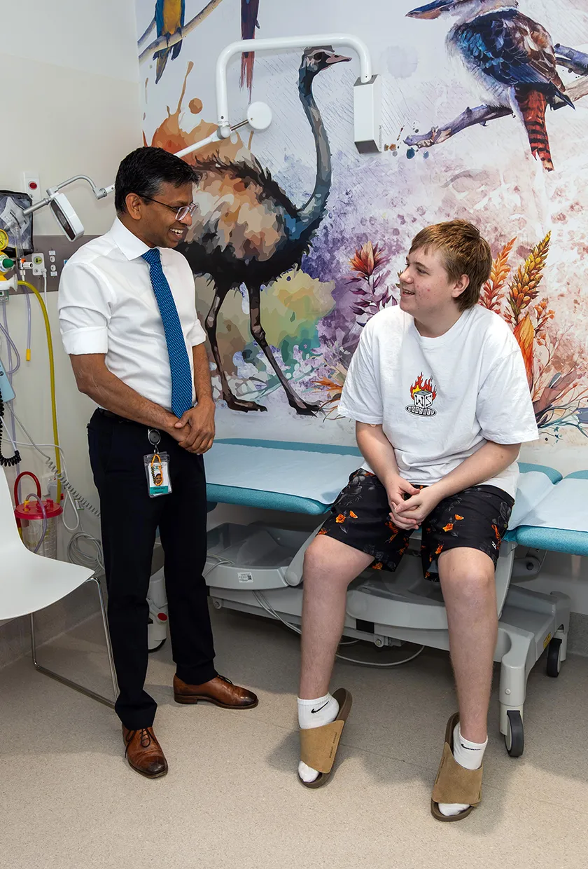 An oncology clinician sitting with an adolescent male patient in a clinic room.