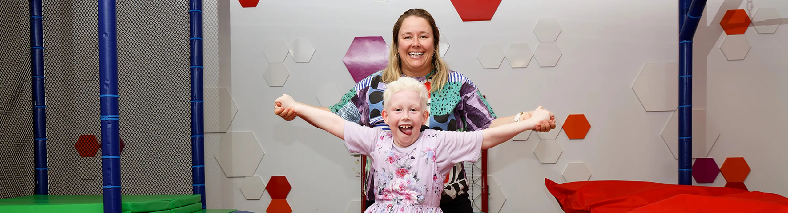 a young girl sticking her tongue out, being supported from behind by an occupational therapist.