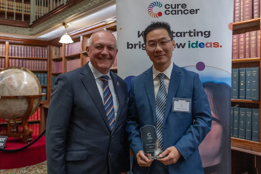 Two men standing side by side, one holding an award