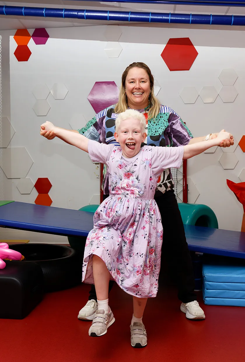 girl smiling with tongue out holding hands with occupational therapist.