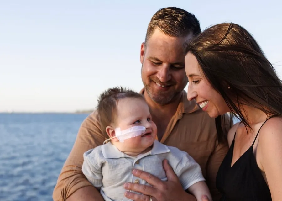 A baby being held by his dad, smiling up at his mum